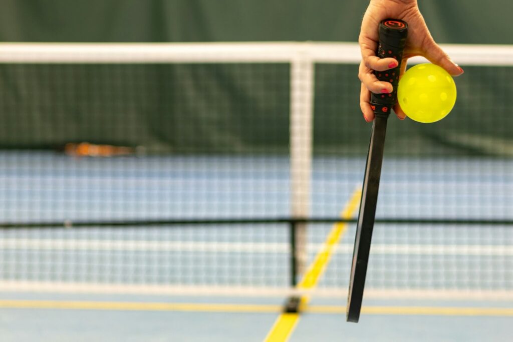 Person holds a pickleball paddle and ball while approaching the court. 