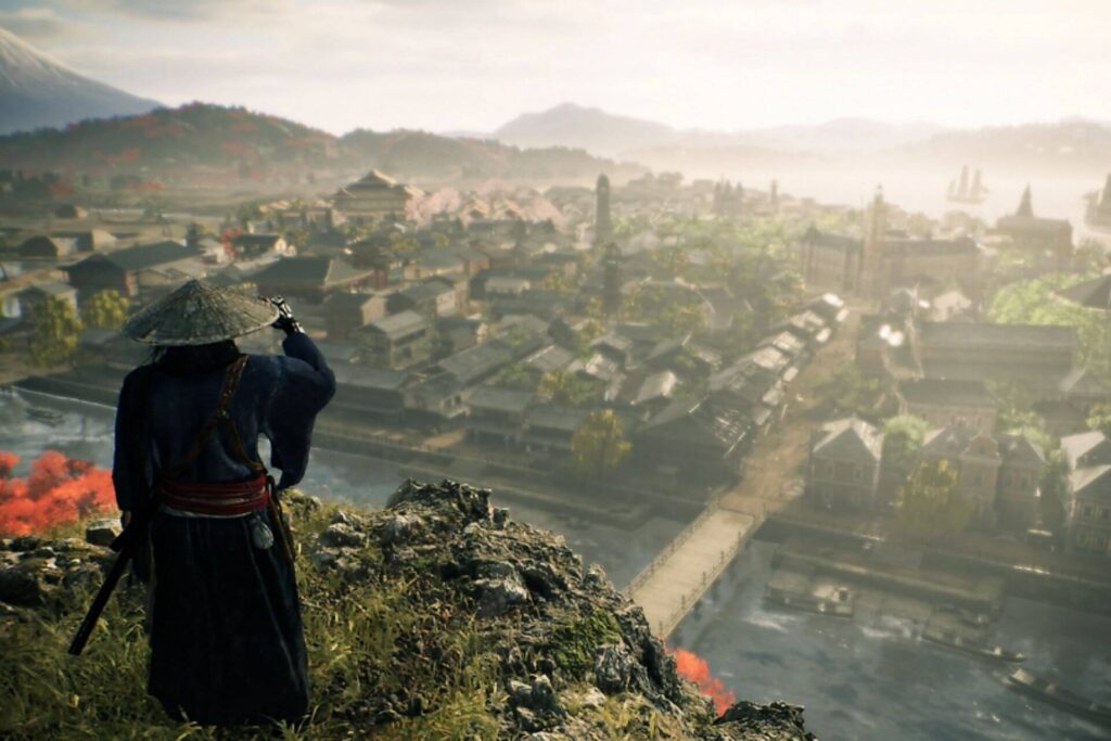 A person wearing a traditional Asian conical hat and blue robe standing on a hill overlooking an ancient Japanese town with a river running through it, mountains in the background, and boats on the water.