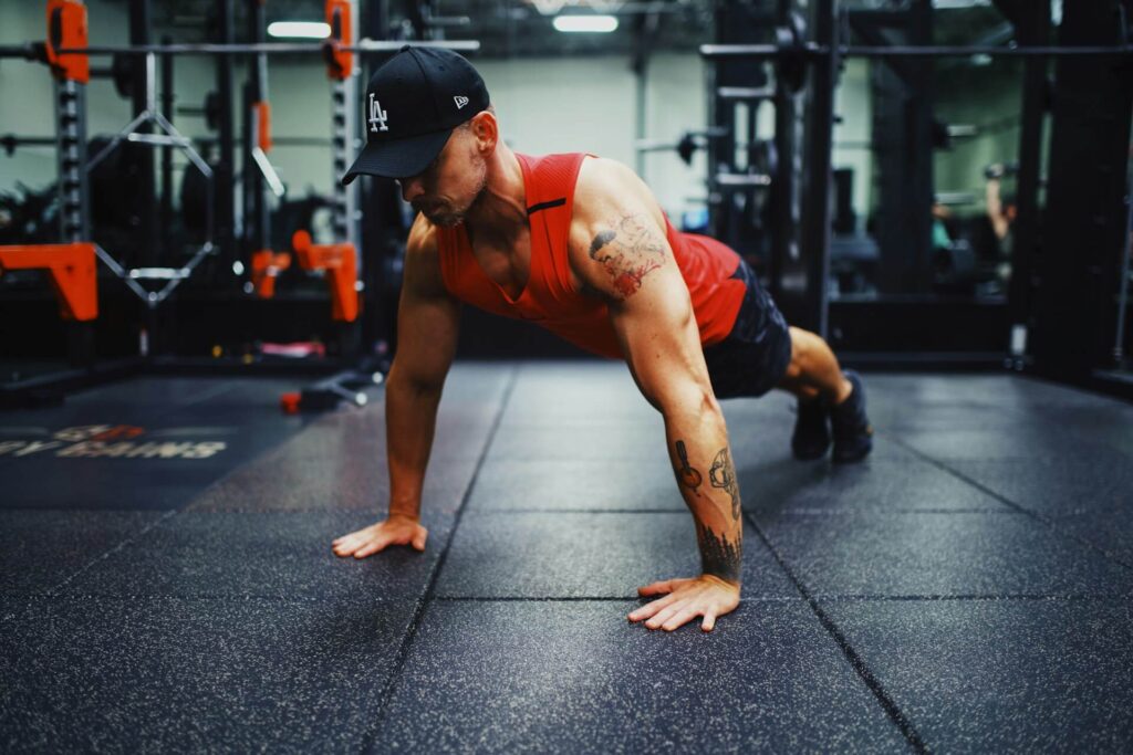 Man in a red tank top does a pushup in a gym