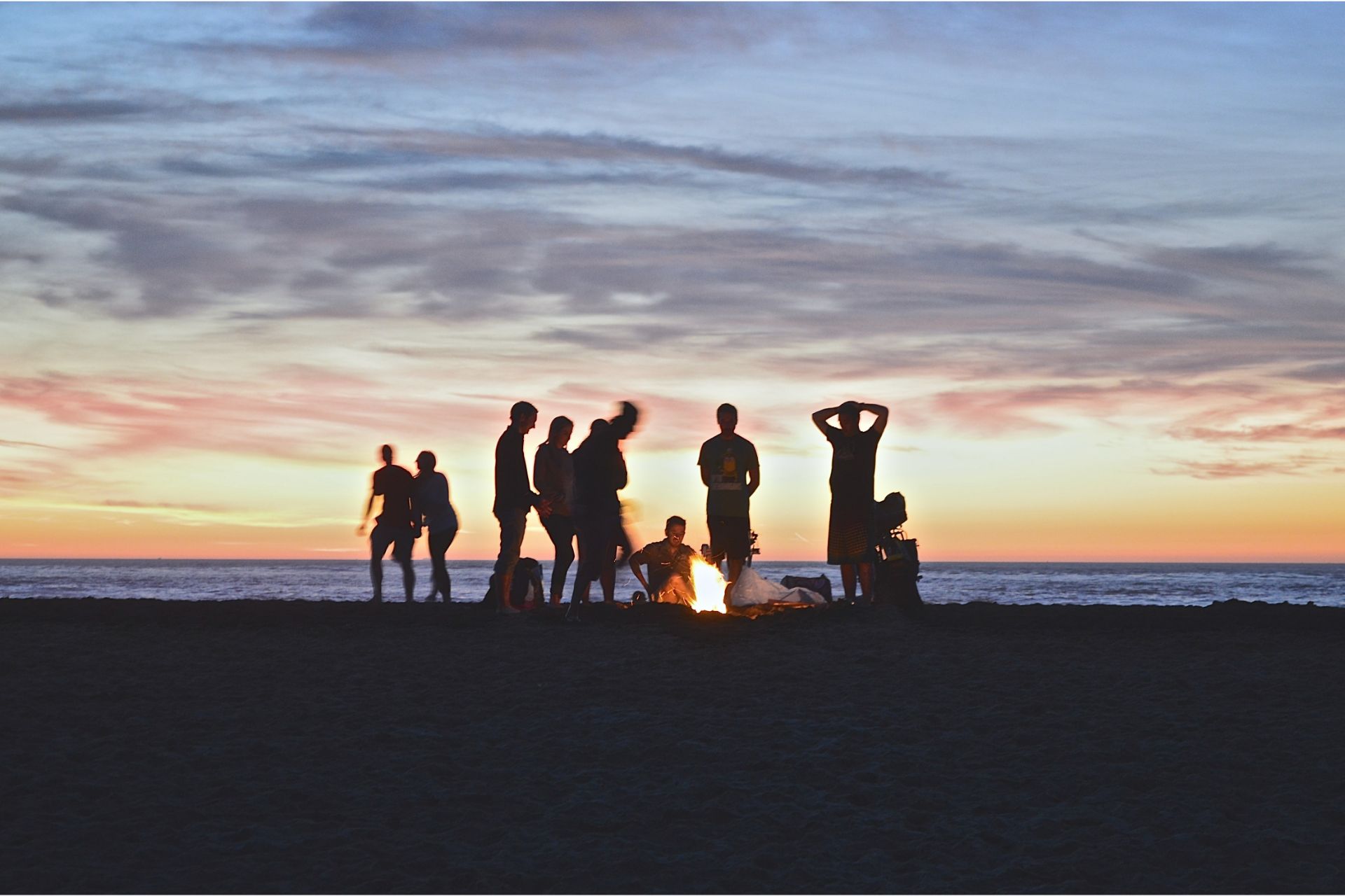 Group of people standing on a beach during a sunset.