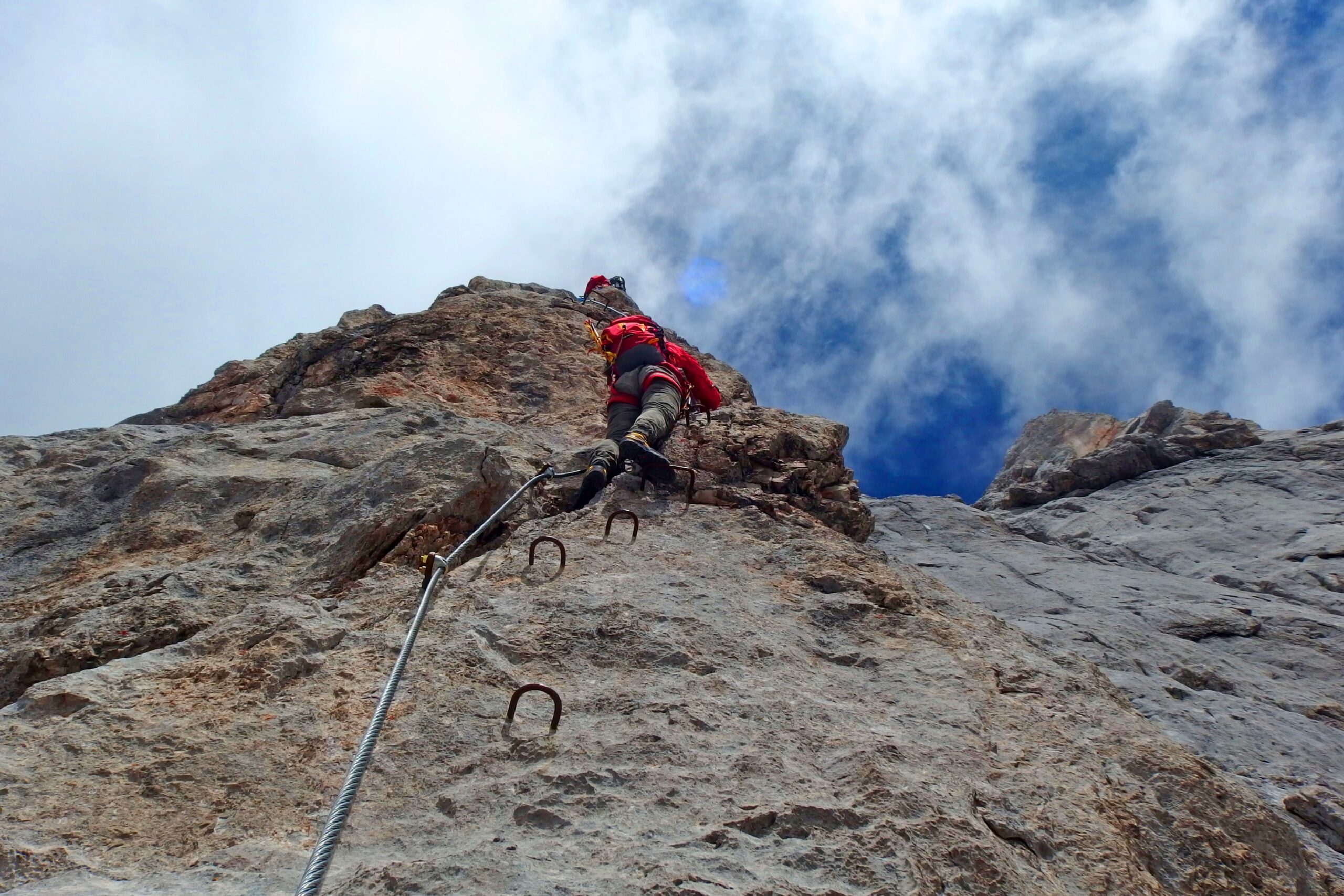 Image looking up at a person climbing a vertical via ferrata trail