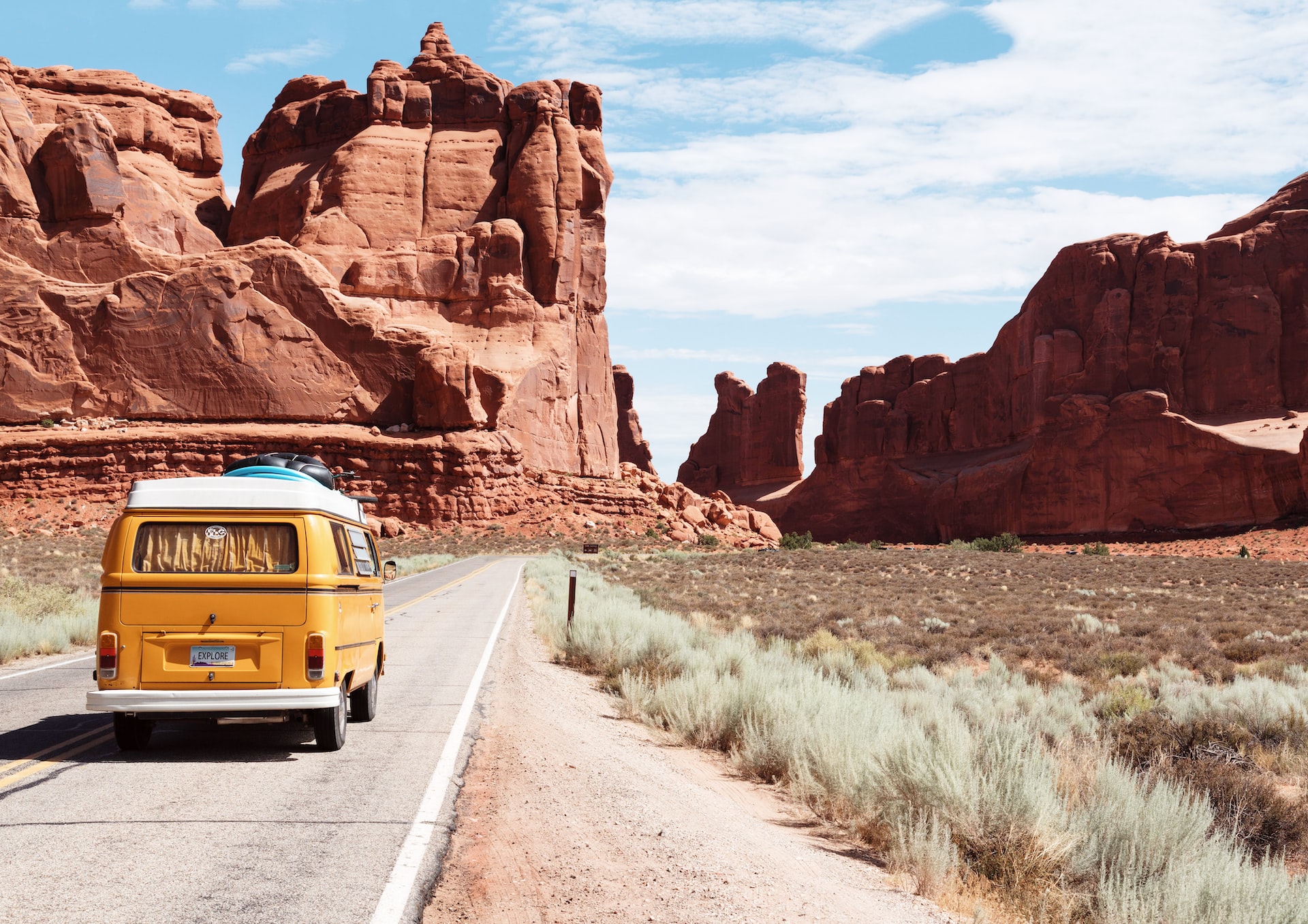 Yellow van traveling down a road in the desert.