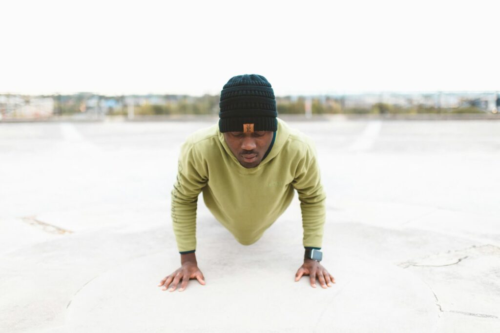 Man in a green sweatshirt doing a pushup on pavement