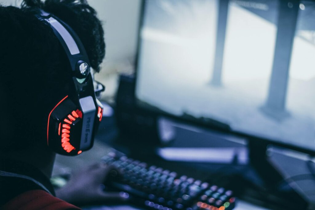 A guy wearing red headphones looks at a computer screen while playing an unknown game